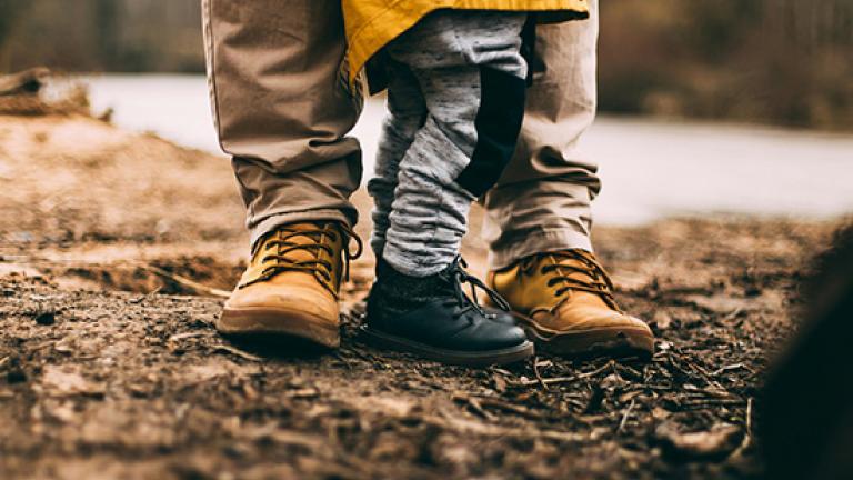 view of adult feet and child in boots standing in dirt